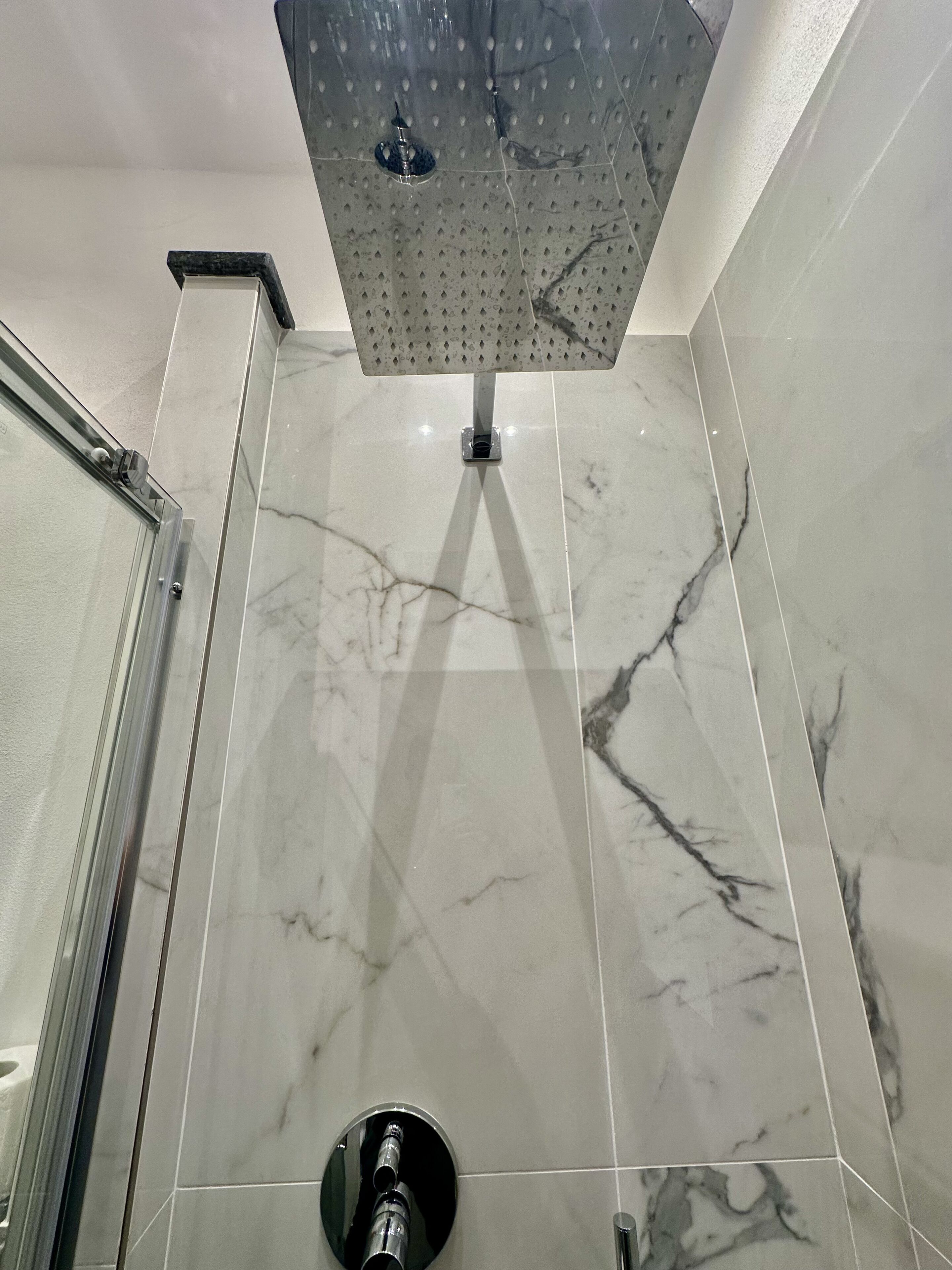 Bagno con doccia, piastrelle in marmo e porta in vetro.