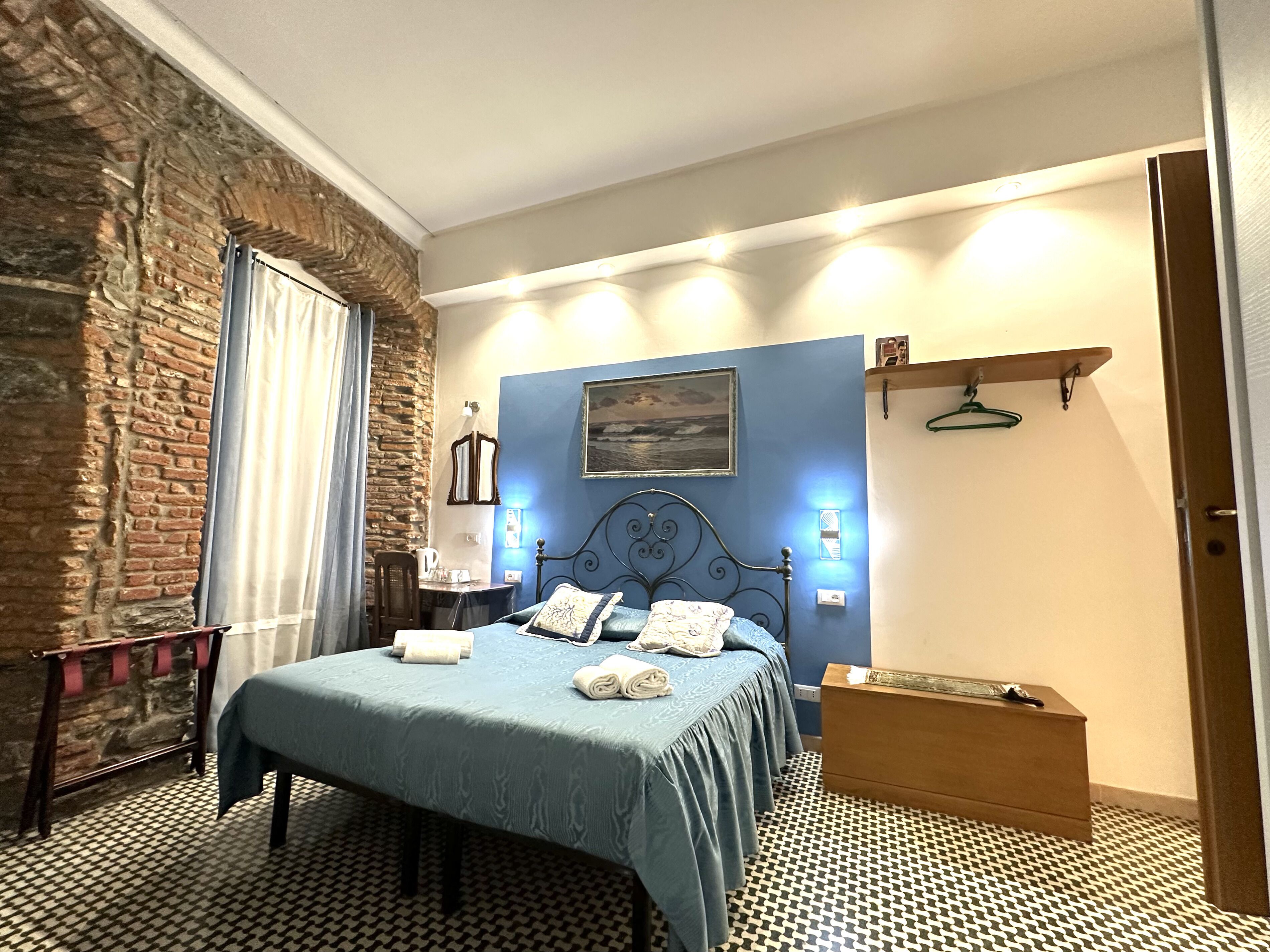 Ein Schlafzimmer mit Bett, Kommode, Nachttisch, Lampe, einem Gemälde und einer Ziegelwand.