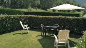 A grassy outdoor area with a table and chairs, a white umbrella, and a view of a mountain range. - Appartamento Con Giardino (Villeneuve)