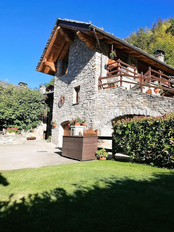 A stone building with a wooden balcony, surrounded by greenery.
