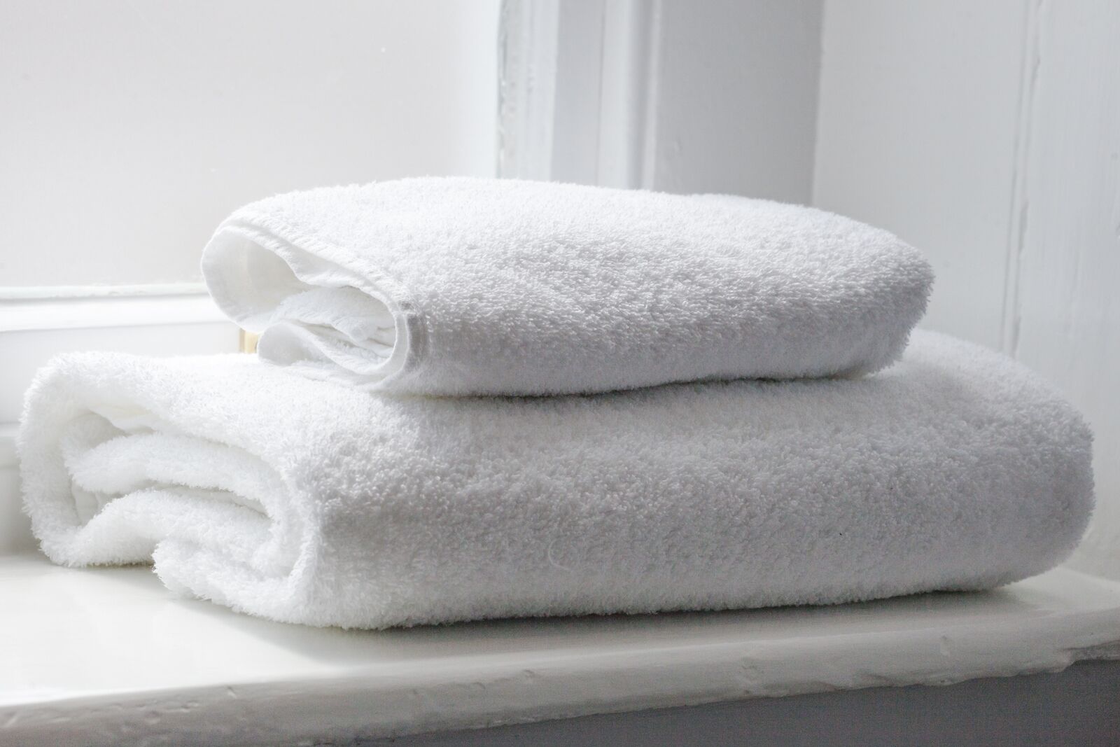 Two white towels stacked on a white surface.