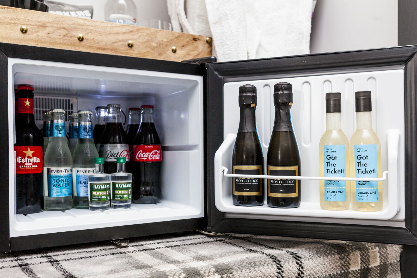 A mini-fridge with various beverages including Estrella, Diet Coke, Coca-Cola, tonic water, and Prosecco DOC.