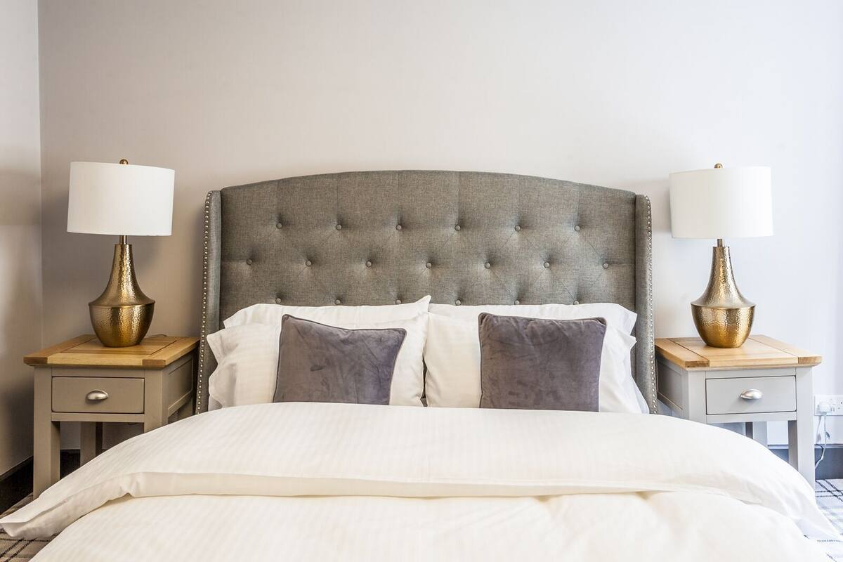 A neatly made bed with a tufted headboard, two bedside tables with lamps, and a simple nightstand drawer.