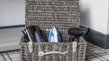 A wicker basket with a handle containing a kettle, a blue and white mug, and a black hairdryer.