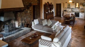 A cozy living room with a stone fireplace, a sofa set, and a dining area with a wooden table. - Podere Le Rote Private Farmhouse (Castelnuovo di Val di Cecina)