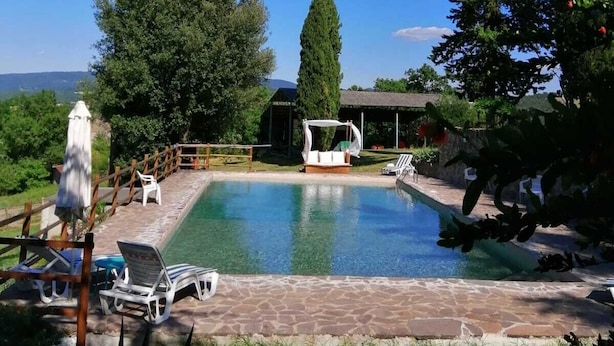 A swimming pool with lounge chairs and a covered seating area, surrounded by trees and a stone deck. - Podere Le Rote Private Farmhouse (Castelnuovo di Val di Cecina)