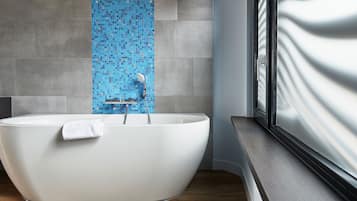 A modern bathroom with a freestanding bathtub, a blue mosaic wall, and a window with a view of a building.