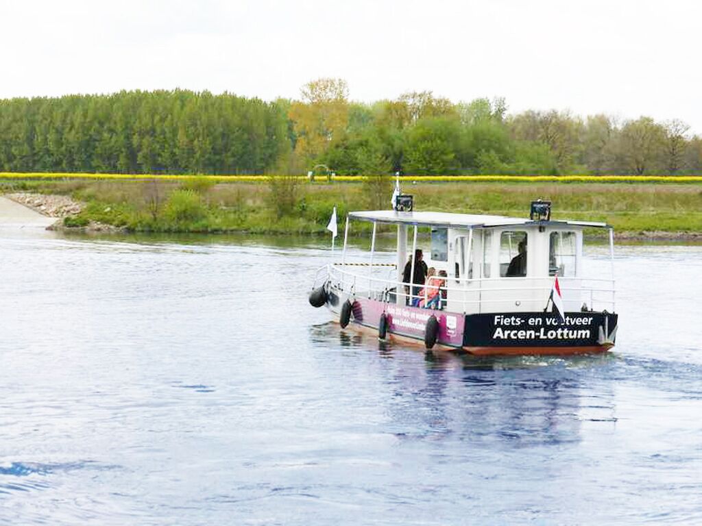 Un bote con el nombre "Fiets-en Vlootje" en el costado, flotando sobre el agua con un área boscosa al fondo.
