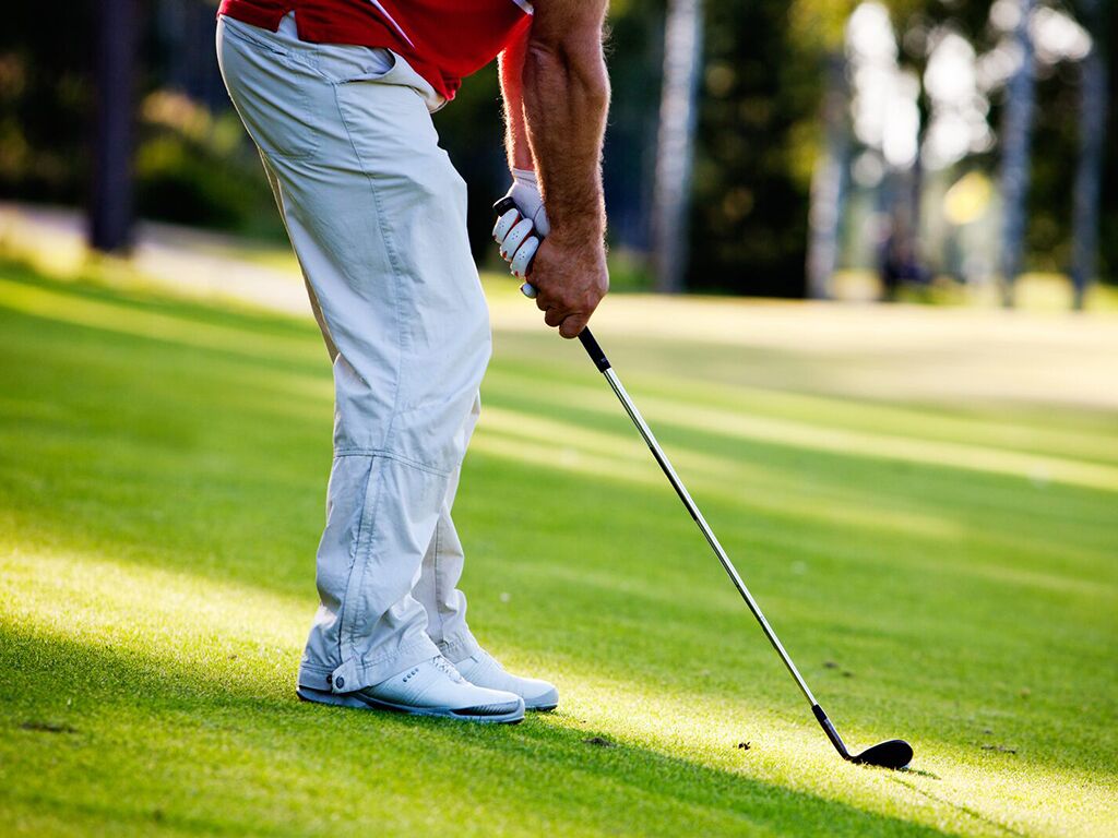 A person in white pants and a red shirt preparing to put a golf ball.