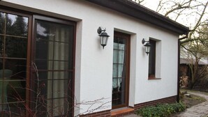 A white building with large windows and two wall-mounted light fixtures. - Ferienhaus Blütenzauber (Lübbenau/Spreewald)