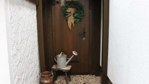 A wooden door with a wreath, a lantern, and a watering can on a small stool. - Ferienhaus Blütenzauber (Lübbenau/Spreewald)