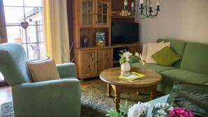 A living room with a green sofa, a green armchair, a wooden cabinet, a television, and a chandelier. - Ferienhaus Blütenzauber (Lübbenau/Spreewald)