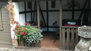 A covered porch with a wooden table and chairs, a potted plant with red flowers, and a rustic wooden stool. - Ferienhaus Blütenzauber (Lübbenau/Spreewald)
