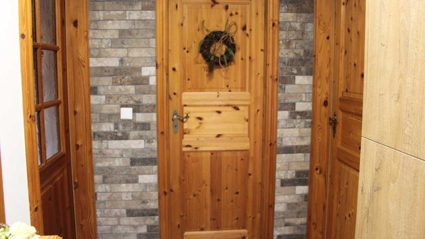 A wooden door with a wreath, set in a hallway with brick walls and wooden doors. - Ferienhaus Blütenzauber (Lübbenau/Spreewald)