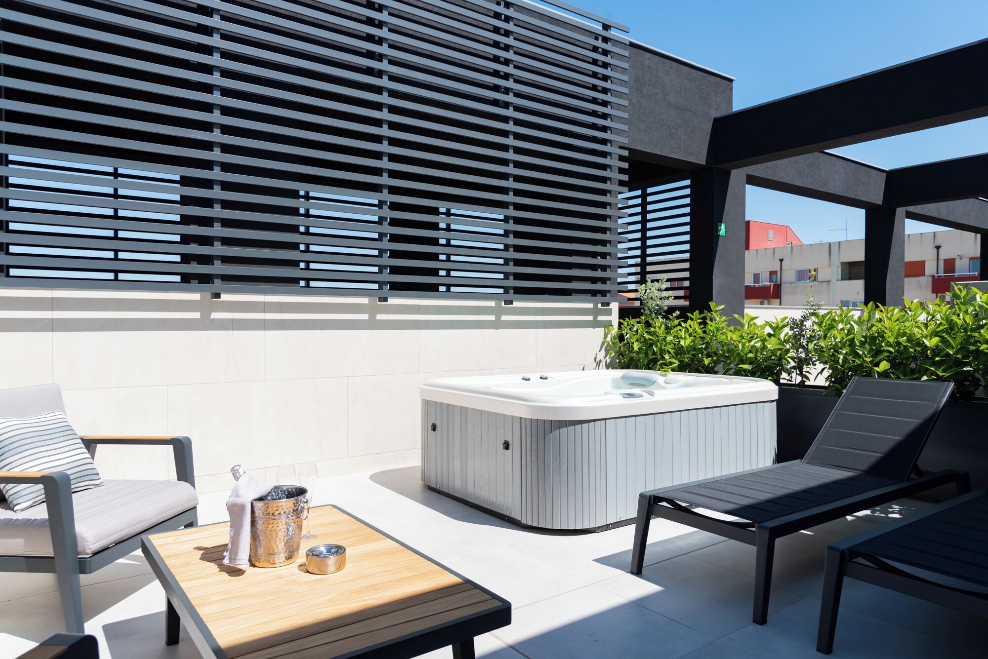 Ein moderner Außenbereich mit Whirlpool, Liegestühlen und einem Holztisch mit einem Getränkebehälter.