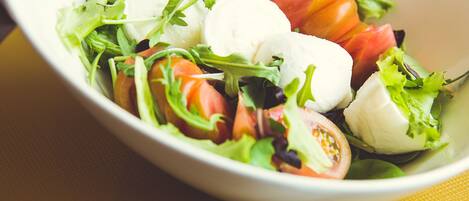 A white bowl of salad with various greens, tomatoes, and mozzarella on a yellow napkin.