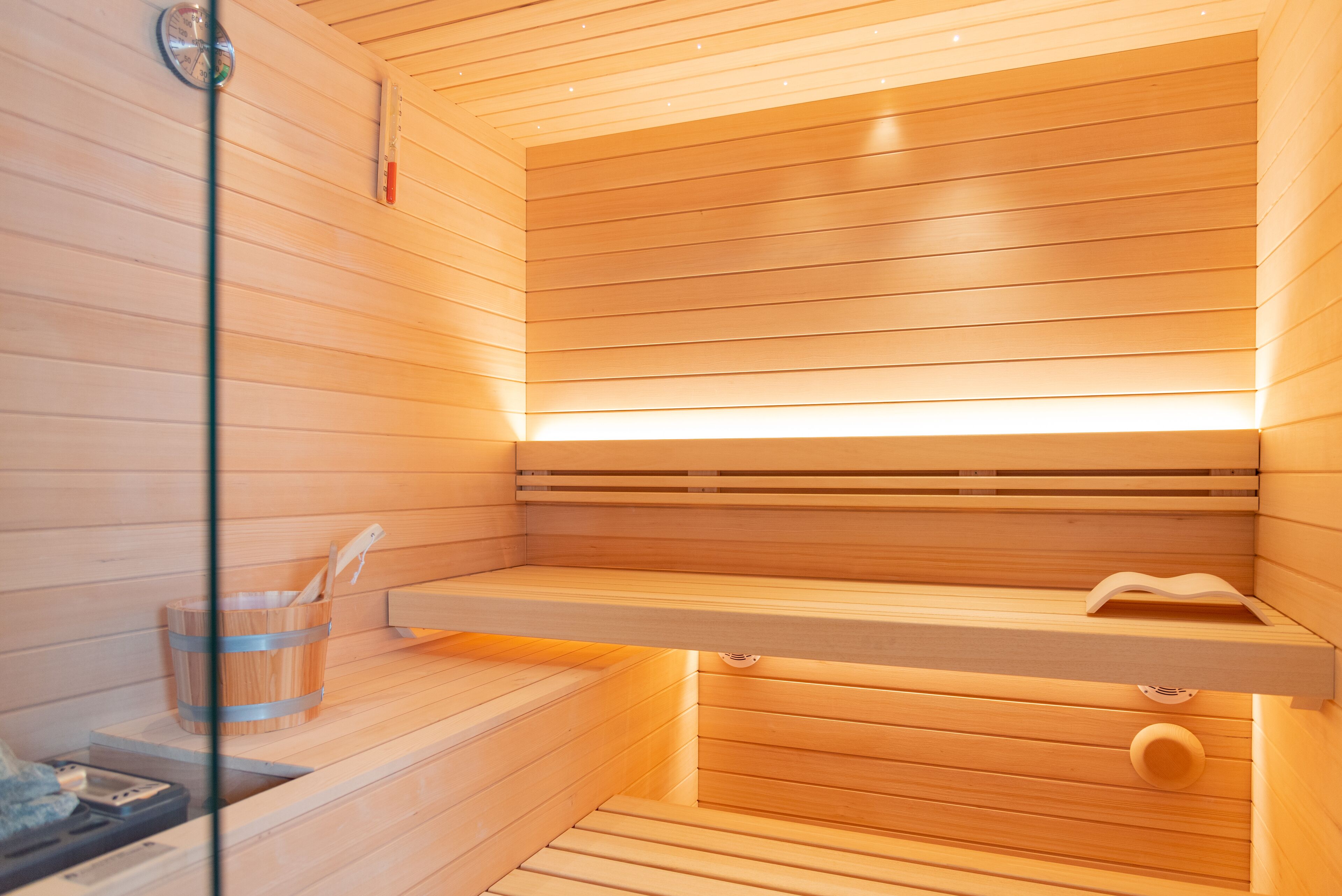 Eine Sauna mit Holzlamellen, einer Holzbank, einem kleinen Holzfass und einem Glasbehälter.