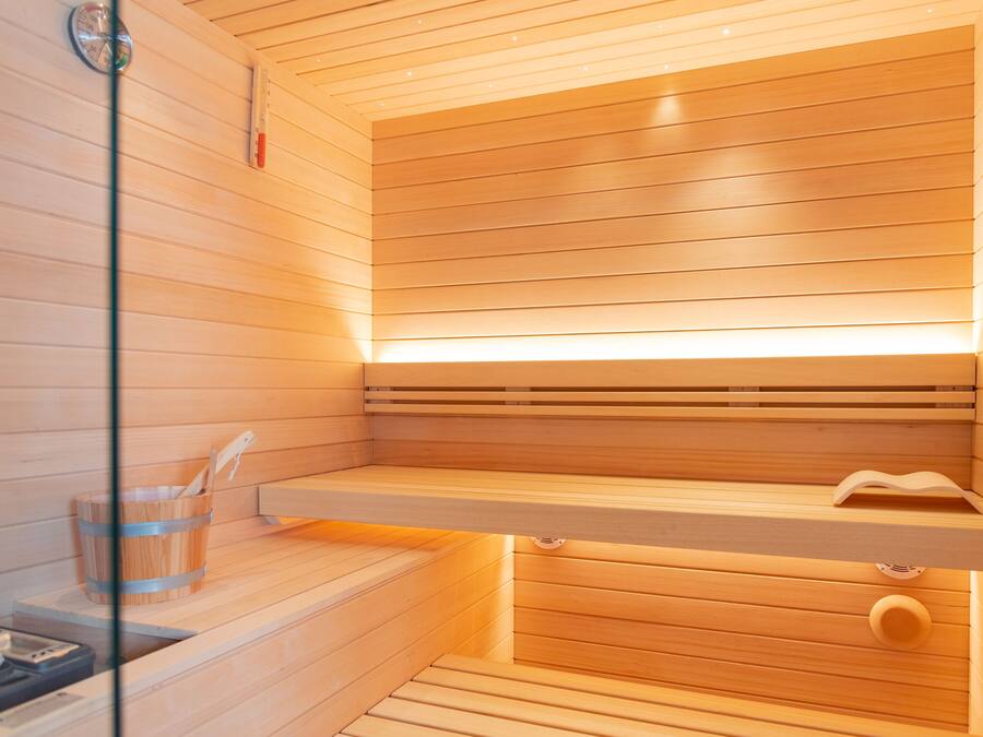 A sauna with wooden slats, a wooden bench, a small wooden bucket, and a glass container.