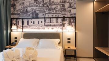 A hotel room with a large bed, two bedside lamps, a nightstand with a phone, and a wall-mounted artwork depicting a cityscape.