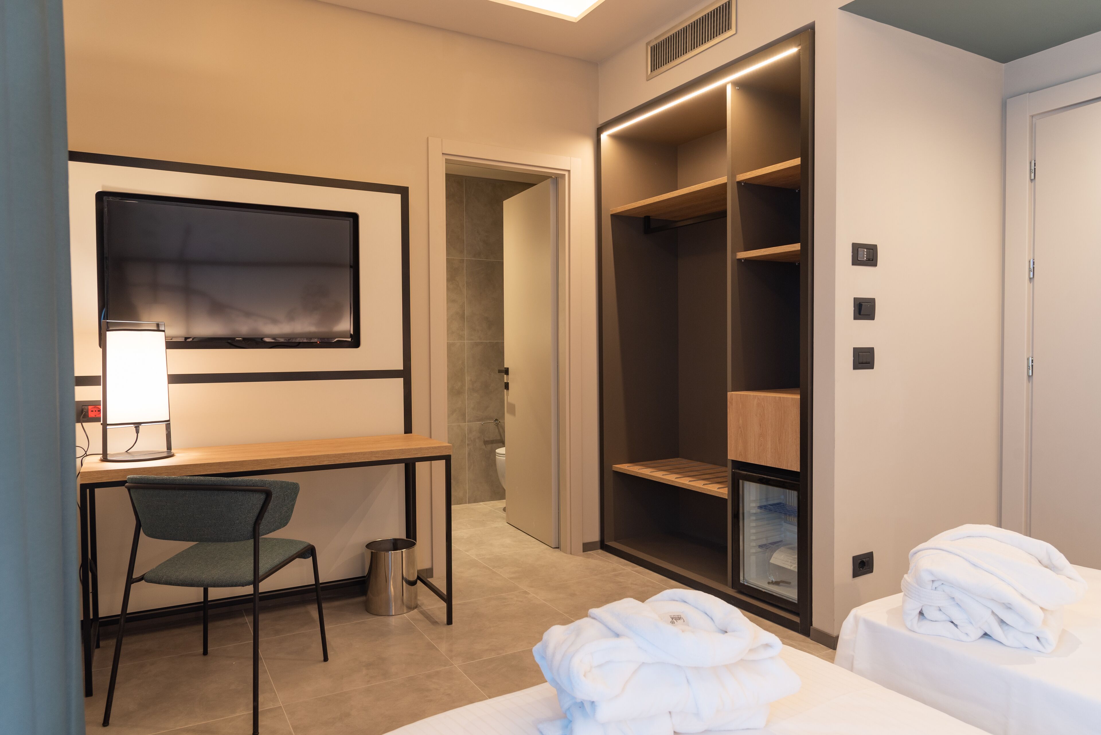 Une chambre d’hôtel équipée d’un bureau, d’une chaise, de deux lits, d’une armoire et d’une salle de bain.