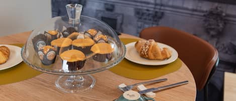 Una mesa con un expositor de vidrio para pasteles con cupcakes, una tetera y un plato con un croissant.
