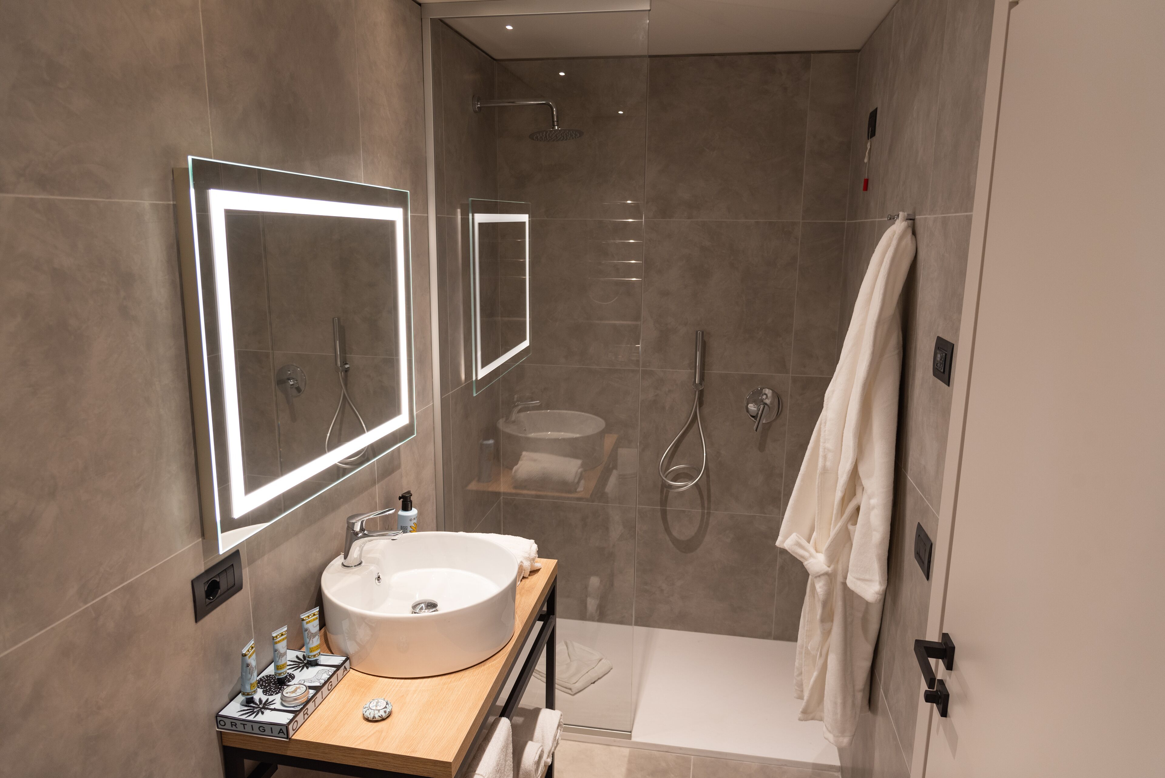 A modern bathroom with a large mirror, a sink, a shower, and a towel rack.