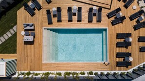 Vue aérienne d’une piscine sur le toit, avec plusieurs chaises longues et un petit espace aménagé avec une table.