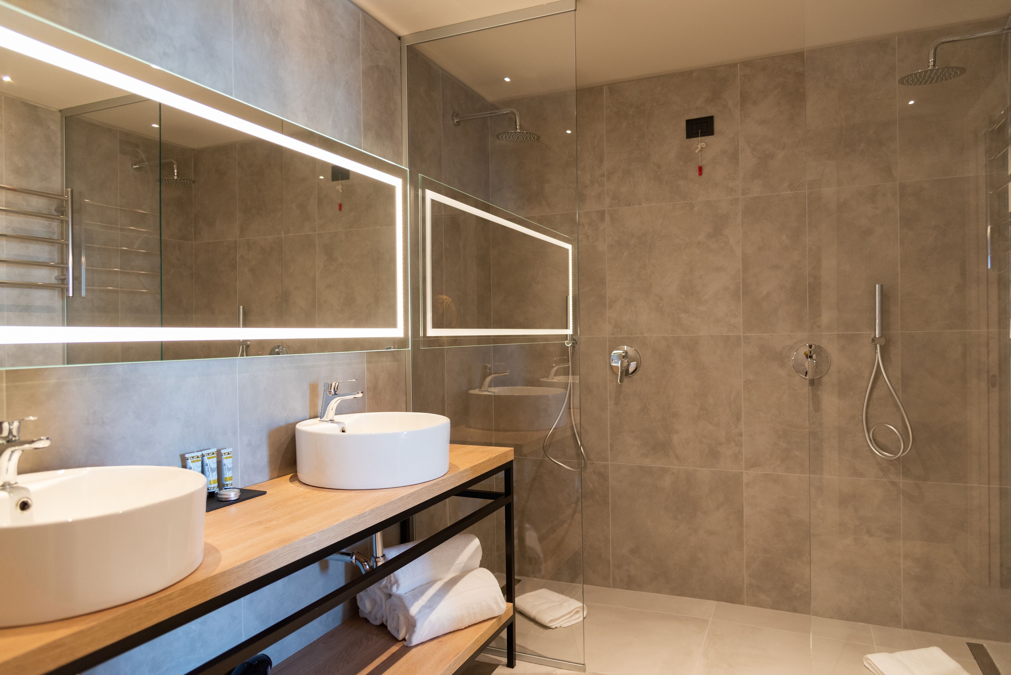 Een moderne badkamer met twee wastafels, een douche met glazen wand en een grote spiegel.