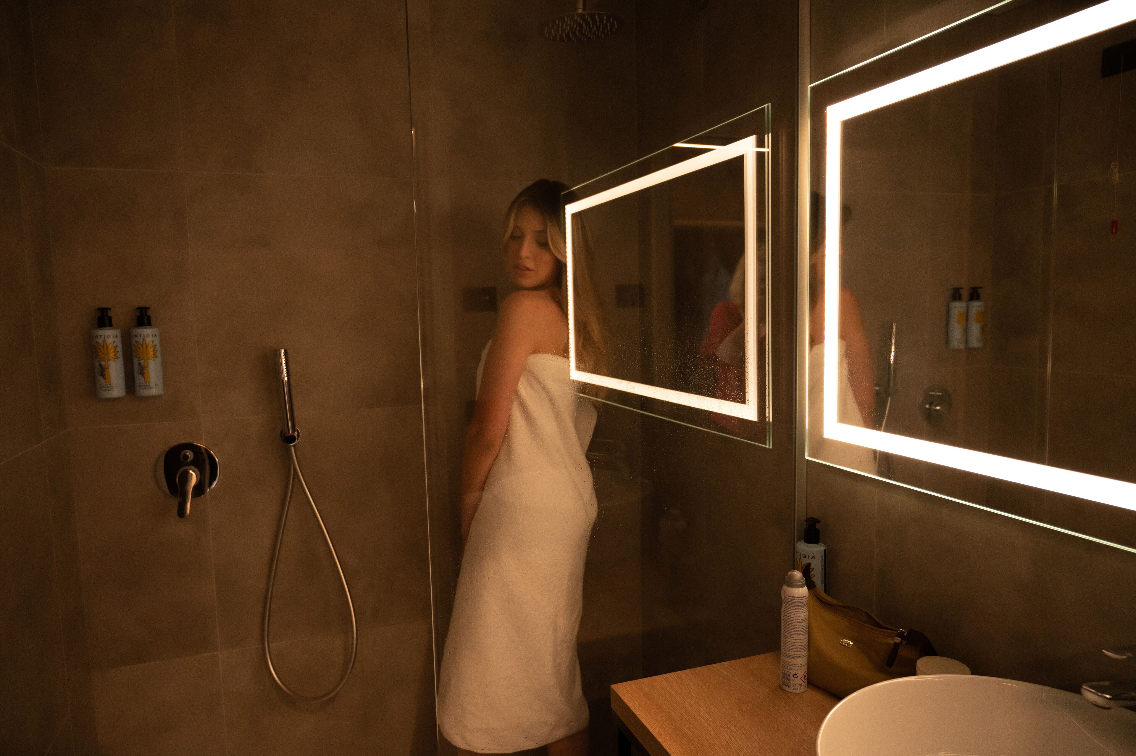 Ein Badezimmer mit einer gläsernen Duschkabine, einem Spiegel mit LED-Beleuchtung und Pflegeprodukten auf der Ablagefläche.
