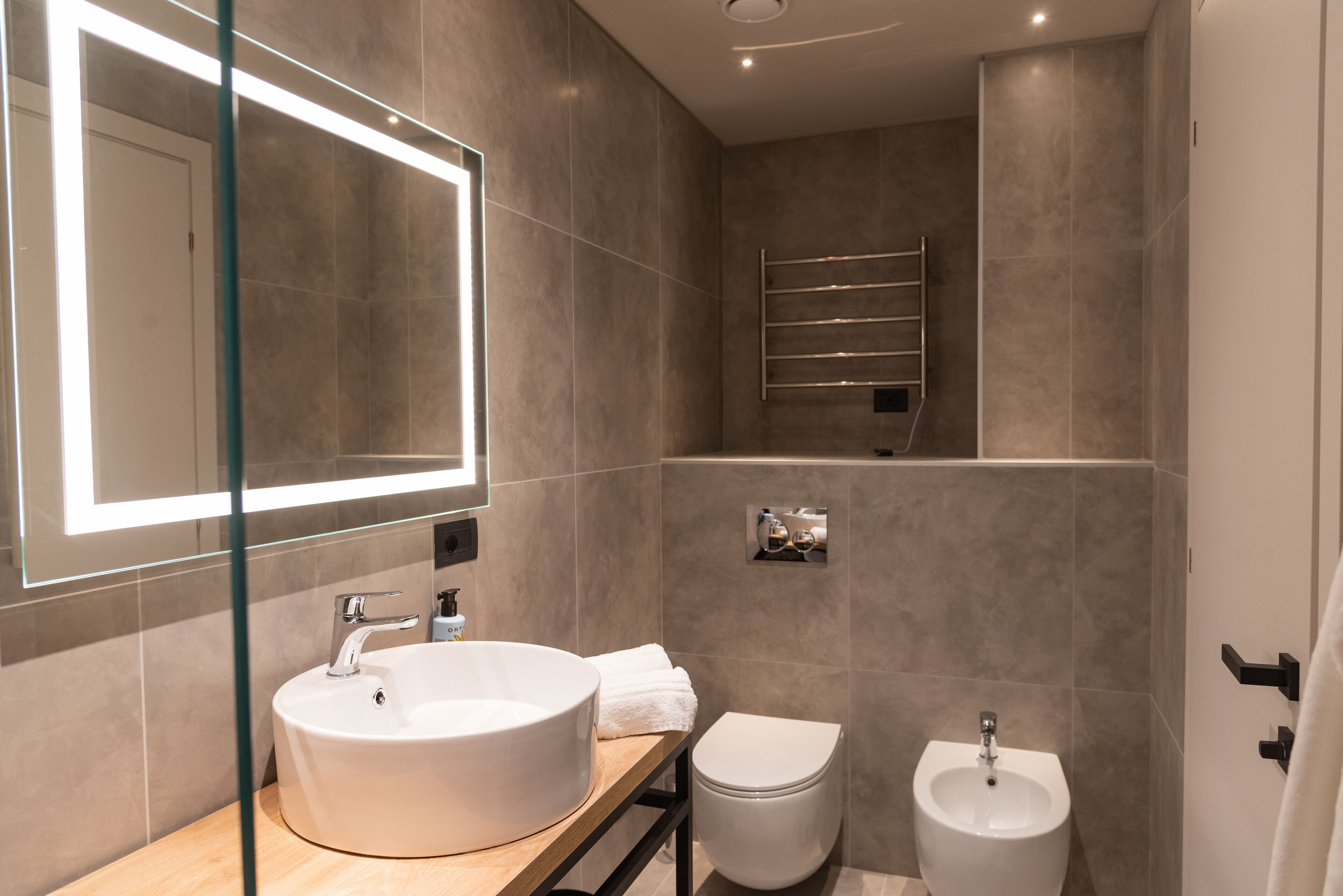 A modern bathroom with a large mirror, a round sink, a toilet, and a bidet.