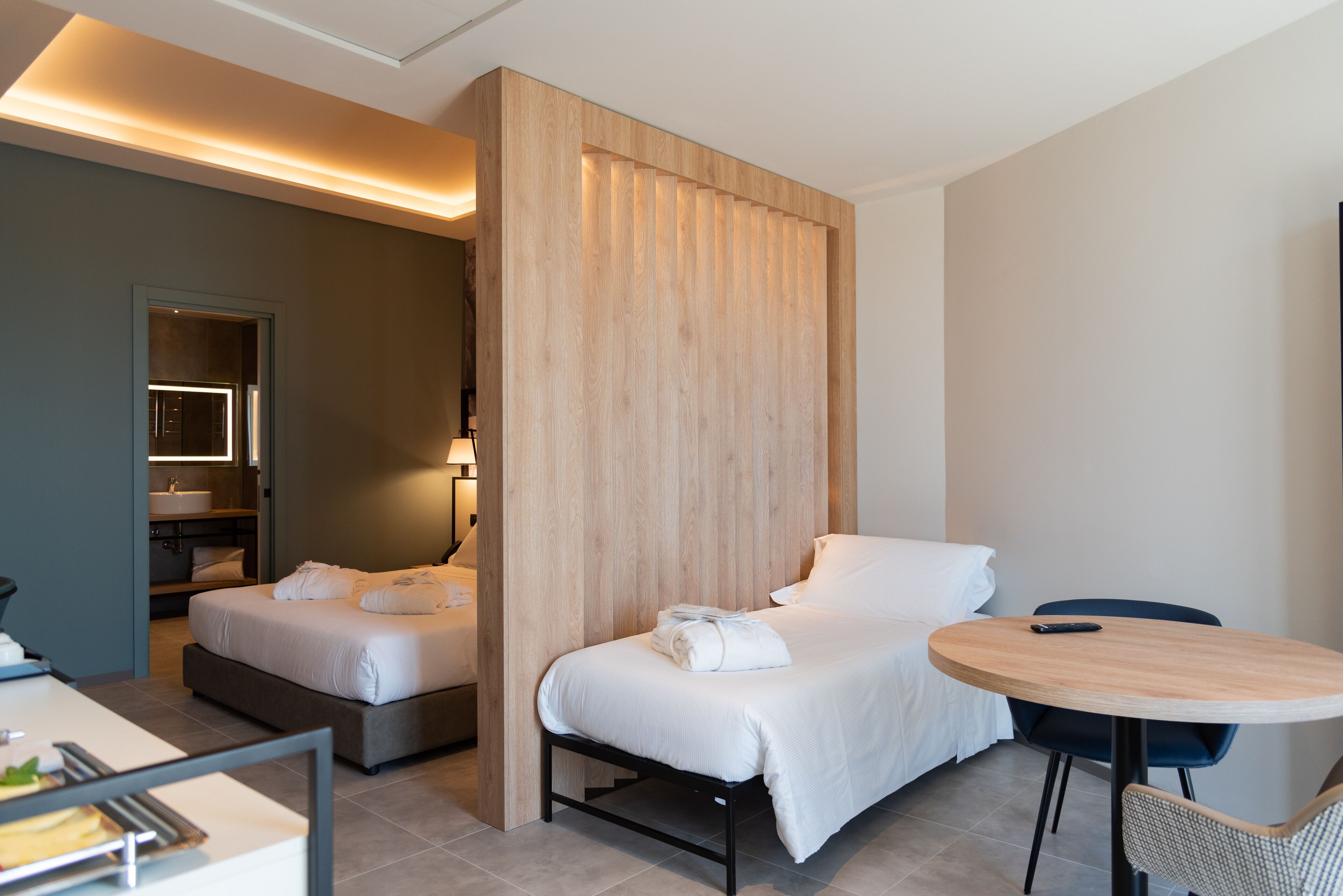 A modern hotel room with a bed, bedside table, and a small round table with chairs.