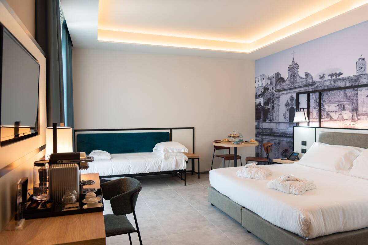 A hotel room with two beds, a desk with a coffee maker, a chair, and a wall mural.