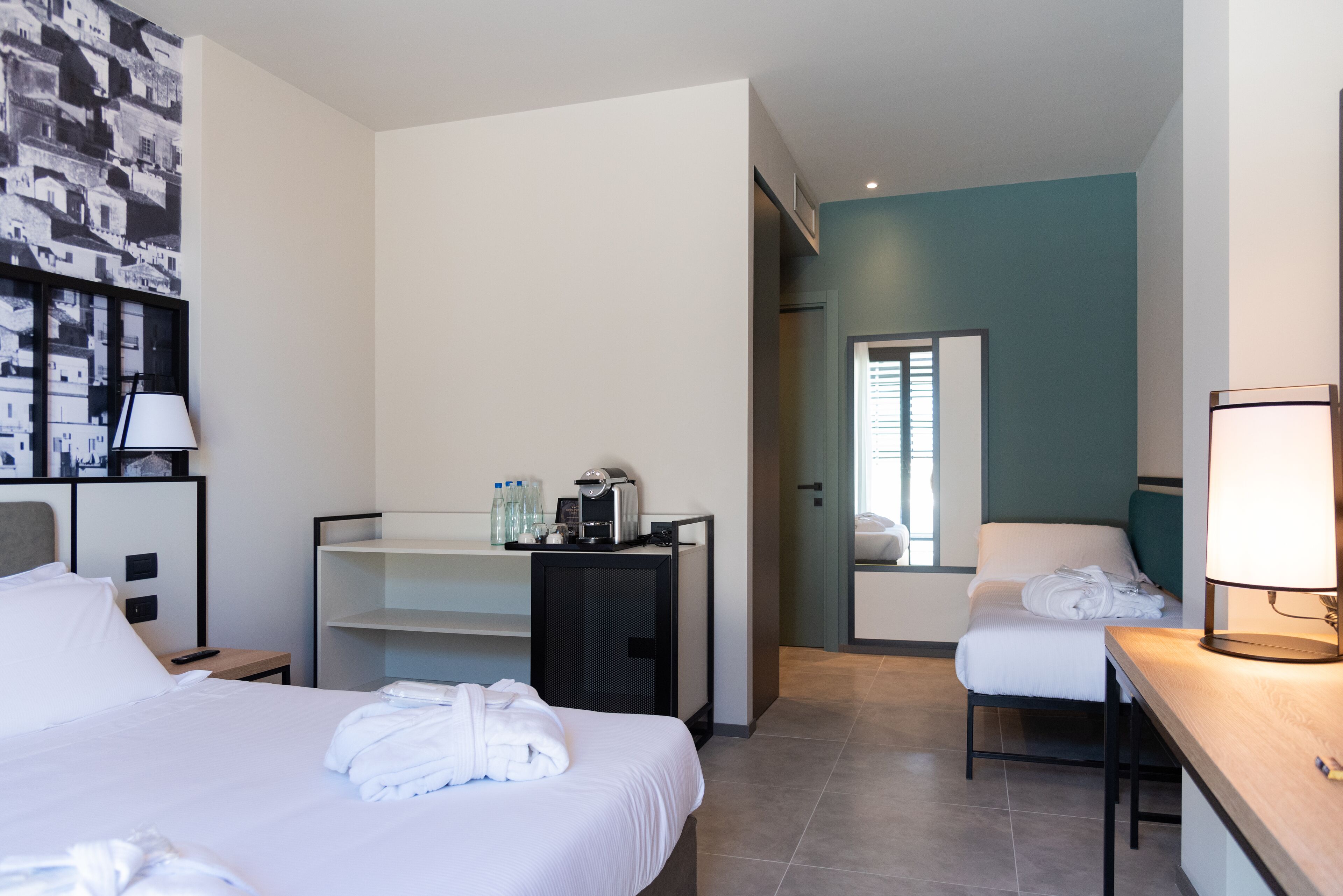 A hotel room with a bed, a desk, a chair, a mirror, and a wardrobe.