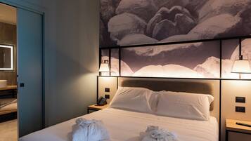 A hotel room with a large bed, a headboard with a mountain landscape mural, bedside lamps, and a nightstand with a phone and a remote control.