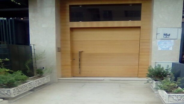 Un'ampia porta in legno con maniglia, affiancata da due fioriere con piante verdi.