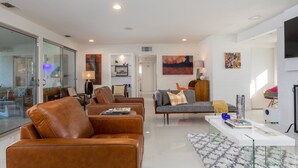 A modern living room with leather sofas, a glass partition, and a flat-screen TV. - Palm Springs Trousdale – Iconic Midcentury Retreat (Palm Springs)