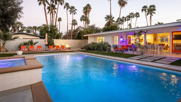 A swimming pool with lounge chairs, palm trees, and a modern house with outdoor seating. - Palm Springs Trousdale – Iconic Midcentury Retreat (Palm Springs)