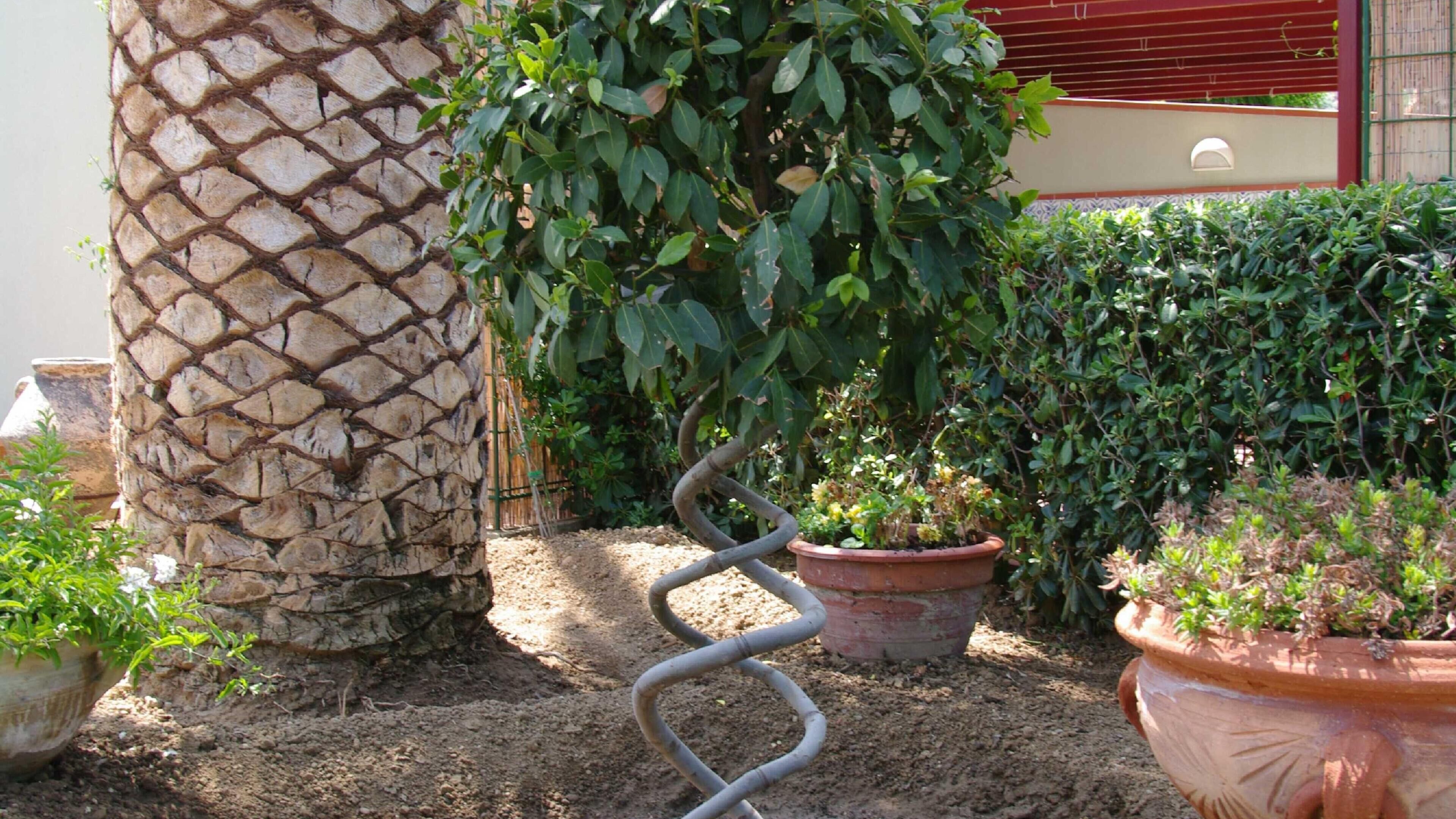 Un jardin avec un mur en pierre, des plantes en pot et une structure en spirale métallique.