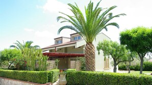 A two-story house with a red roof, surrounded by well-maintained hedges and palm trees. - Relaxing Apartment for 2 People in Residence (Cefalù)