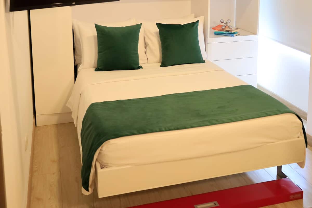 A modern bedroom with a bed, green pillows, a mounted TV, and a red drawer unit.