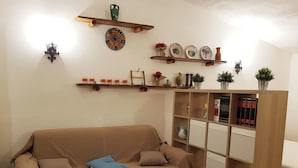 A cozy living room with a beige sofa, a wooden bookshelf, and decorative plates on the wall. - Chalet in the Woods Nestled in the oak Forest in Monterosso Etneo (Aci Sant'Antonio)