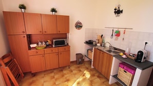 A compact kitchen with wooden cabinets, a microwave, a sink, and various kitchen utensils. - Chalet in the Woods Nestled in the oak Forest in Monterosso Etneo (Aci Sant'Antonio)