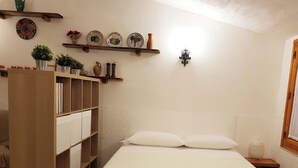 A bedroom with a bed, a wooden wardrobe, a shelf with decorative plates, and a wall-mounted light fixture. - Chalet in the Woods Nestled in the oak Forest in Monterosso Etneo (Aci Sant'Antonio)