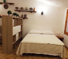 Un dormitorio con cama, un armario de madera, una estantería con platos decorativos y un aplique de pared.