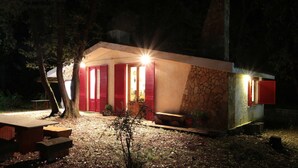 A small, single-story building with red shutters, a stone facade, and a well-lit entrance. - Chalet in the Woods Nestled in the oak Forest in Monterosso Etneo (Aci Sant'Antonio)
