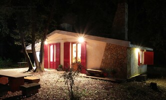 Un edificio pequeño de un piso, con contraventanas rojas, fachada de piedra y una entrada bien iluminada.