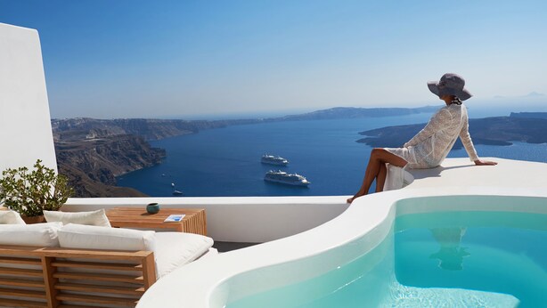 A person relaxing by a pool with a view of the sea and boats. - Native Eco Villas (Santorini)