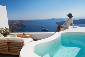 A person relaxing by a pool with a view of the sea and boats. - Native Eco Villas (Santorini)