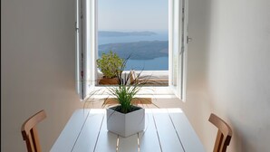 A dining area with a table and chairs, a potted plant, and a view through an open door. - Native Eco Villas (Santorini)
