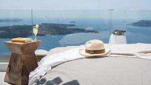 A bedroom with a view of the sea, a hat, and a book on a side table. - Native Eco Villas (Santorini)